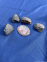 Four unpolished rough stones and one pink and white polished agate slice on blue cloth background