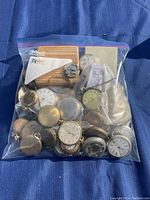 Zip-top bag with assorted pocket watches and parts on blue fabric