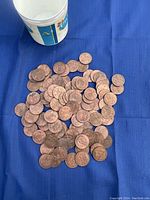 Bucket with approx. 80 copper tokens scattered on blue cloth, showing size and quantity.