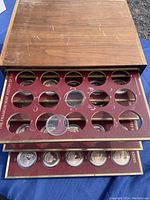 Top view of wooden storage case with multiple trays containing bronze medallions in red maroon inserts with circular cutouts