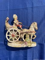 Porcelain figurine of horse pulling carriage with seated driver shown against blue background.