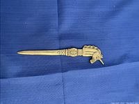 Photo of metal letter opener with detailed unicorn head design and Shelley engraving on a blue cloth background