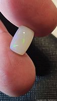 Close-up photo of the rectangular cabochon cut Ethiopian opal held between fingers showing smooth polished surface with green color flashes.