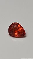 Close-up image of the fire orange pear-shaped sapphire highlighting its facets and clarity.