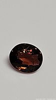 Oval cut Padparadcha tourmaline gemstone lying on a white background showing deep pinkish-peach tone with facets visible.