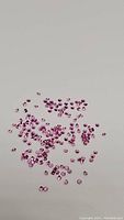 Image showing scattered small bubblegum pink sapphires, round faceted, on a plain background.