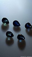 Six polished pear cut sapphires showing deep blue and blue-green color under light with translucent clarity.