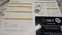 Photo of the GRA certification grading report showing ring specifications: 1 carat weight, D color, VVS1 clarity, excellent polish and symmetry for the moissanite gemstone.