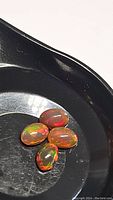 Four oval-shaped natural chocolate opal gemstones on black dish surface showing multicolor splashes of red, green, yellow, orange.