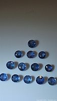 Front view of 14 loose round cut denim blue sapphires arranged in rows showing size and color consistency.