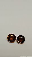 Two round faceted fire orange tourmaline gemstones on a plain background, showing deep orange color and clarity.