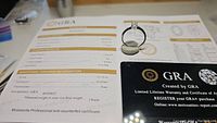 Photo showing the GRA grading certificate with details of the moissanite, alongside the ring.