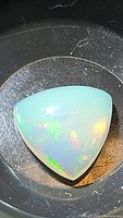Close-up photo of natural AAA Ethiopian opal in trillion cabochon cut under lighting to show rainbow flash.