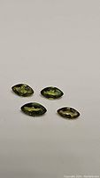 Four marquis cut natural sapphires placed on white background showing multicolored green-yellow hues and reflective surfaces.