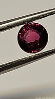 Front view of round cut ruby held in tweezers showing color and facet arrangement.