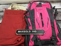 Photo showing red tote bag with cream handles alongside pink and gray backpack with black straps and accents placed on a wooden surface.