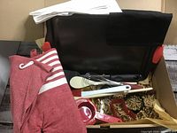 Full view of the baking set in a box showing apron, oven mitt, baking pan, measuring spoons, whisk, spatula, flipper, cookie cutters, and tea towel.