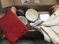 Boxed baking set showing proofing baskets, measuring cups, whisk, scraper, apron, and tote bag inside cardboard box with packing.