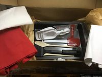 Top-down photo of boxed baking set showing baking pan, measuring cups, red spatula, wooden spatula, black flipper, and boxed utensils with white tea towel, red apron, and white tote bag nearby.