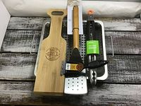 Overview of all BBQ accessories including heavy metal vegetable pan, wooden spatula, metal flipper, tongs, and brush