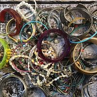 Top-down view of mixed costume jewellery with bracelets, bangles, and beaded pieces arranged on rustic wooden surface.