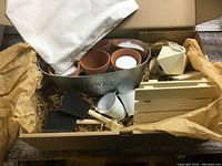 Box open showing all contents: terracotta pots, metal flower container, white metal containers, wooden birdhouse, wooden crate, geometric container, foam paint brushes, and fabric tote bag.
