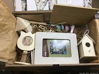 Craft box showing contents including wooden frames, birdhouses, letters, paint jars, and a paintbrush.