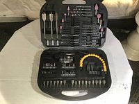 Drill accessory set in open black plastic case showing various drill bits, grinding stones, screwdriver bits, and flexible shaft attachment.