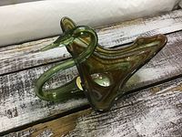 Angle showing the elongated curved neck and flared bowl body with green and amber swirled colors on rustic wood surface.