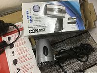Photo of Conair dual voltage hair dryer in its original box and the hair dryer's compact silver and black design with a folding handle.