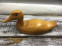 Side profile of hand carved mallard duck showing the full body with polished wood grain and minor nicks
