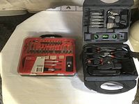 Photo shows two tool kits placed side by side on a white surface. Left is a red case with various rotary tool bits and small accessories. Right is a larger black case containing hand tools arranged neatly in compartments.