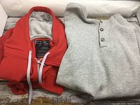 Foot Locker red hoodie folded with gray Tultex pullover sweatshirt next to it on a wooden surface.