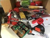 Photo showing various new kitchen utensils including measuring cups, spoons, a brush, tongs, and packaged herb/spice packets inside a cardboard box.