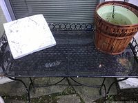 View of the entire metal garden stand with wire mesh top and decorative edges, showing some weathering and slight rust spots.