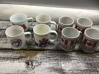 Six ceramic mugs with Canada-themed designs on wooden surface