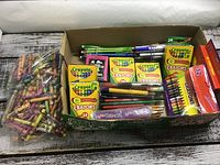Photo showing various boxes of Crayola crayons in 15, 24 and 32 count, loose crayons in a plastic bag, and pens and pencils in green, blue, purple colors.