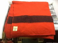 Orange blanket with dark brown horizontal stripe folded showing woven label "Pioneer by Ayers of Lachute".