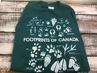 Full front view of green sweatshirt with white animal footprint graphics and 'Footprints of Canada' text.