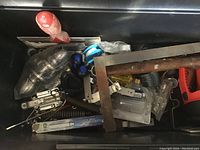 View inside toolbox showing multiple hand tools including screwdrivers, red pry bar, caulking gun, and clamps