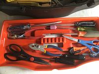 Orange tool tray with scissors, needle-nose pliers, various screwdrivers, and a small metal file arranged inside.