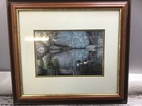 Framed 'Loon' print showing two loons on a reflective water surface with rocks and trees in the background, in wood frame with white matte