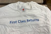 Photo showing white Hanes extra large T-shirt with blue text 'First Class Returns' on front