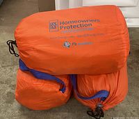 Three orange flood barrier kit bags stacked on top of each other, showing carrying straps and drawstring closures.