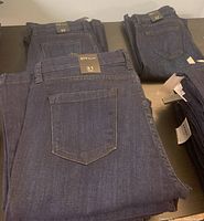Six pairs of dark blue denim jeans folded, showing back pockets and labels, with size tags indicating 31.