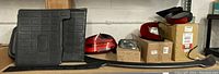 Photo showing automotive parts including black rubber floor mats, red and chrome tail light assemblies, and a long black trim piece