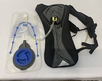 Black and grey Ozark Trail hydration pack with attached clear plastic water reservoir bladder featuring a blue screw cap and drinking tube with valve.