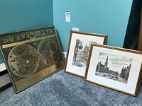 Full view of three framed art pieces: two European prints and one map, arranged on carpet against a wall
