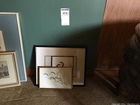 Three framed prints leaning against a wall, partially visible titles and frames.