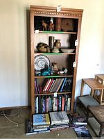 Front view of tall oak look pressboard bookcase with several shelves, displaying books and decorative items (not included).
